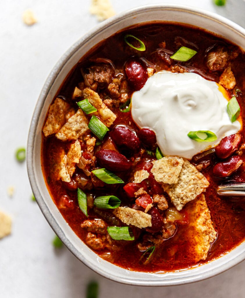 slow cooker chili topped with green onion, corn chips, and sour cream