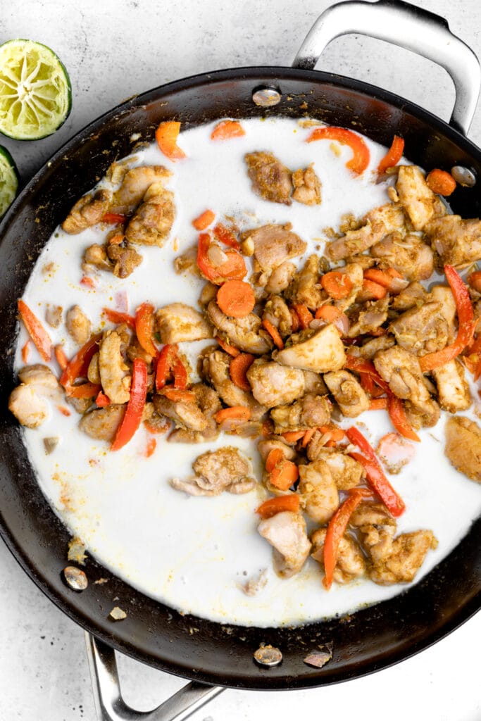 chicken, veggies, coconut milk, and curry paste in black pan