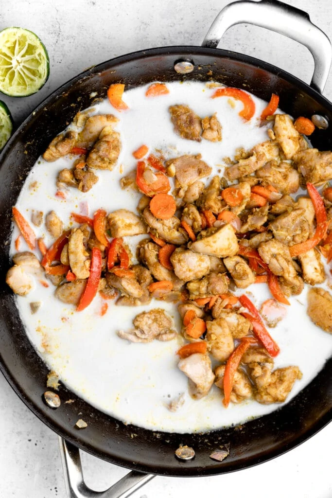 chicken, veggies, coconut milk, and curry paste in black pan