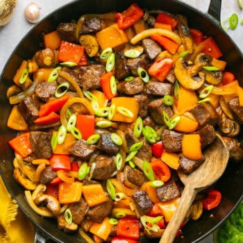 beef tips and peppers in skillet with wooden spoon