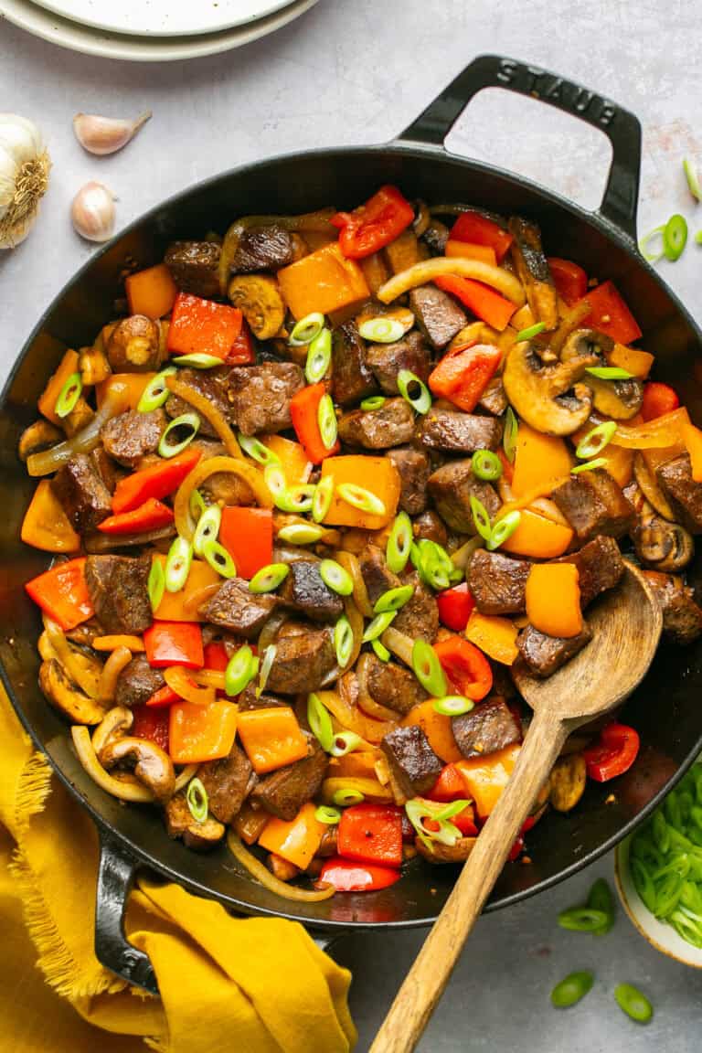 beef tips and peppers in skillet with wooden spoon