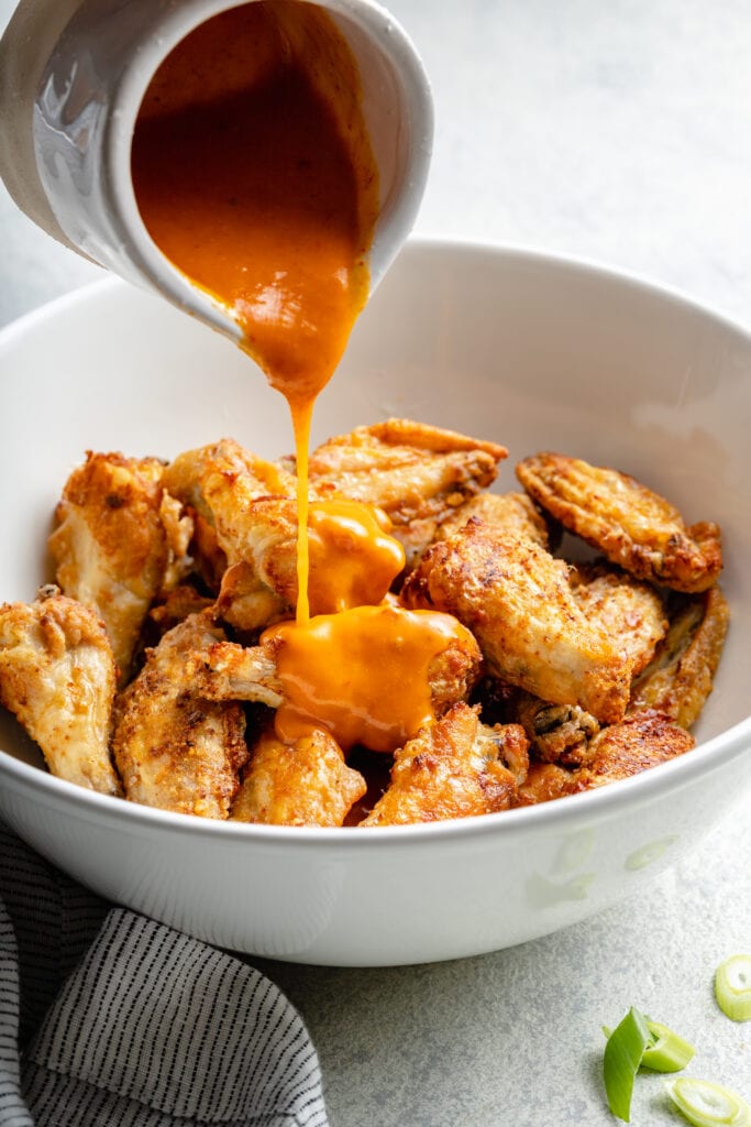 cooked wings being tossed in buffalo sauce
