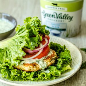 greek chicken burger on a white plate with container of green valley yogurt in the background