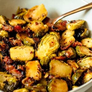 Roasted Brussels sprouts in a white bowl with gold spoon