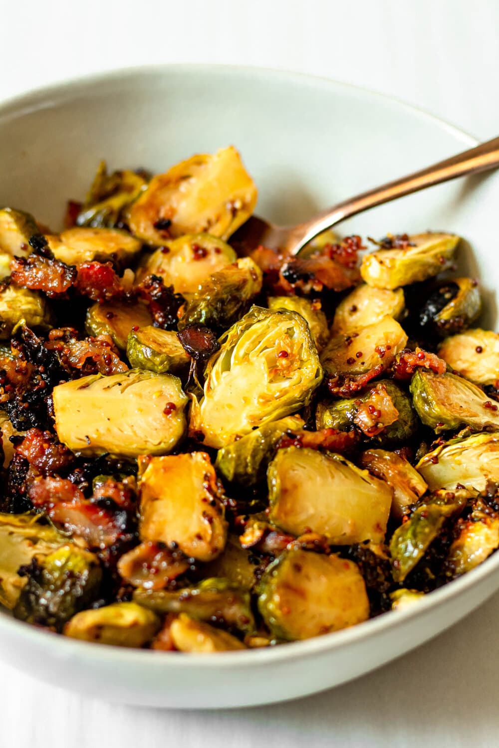 Roasted Brussels sprouts in a white bowl with gold spoon