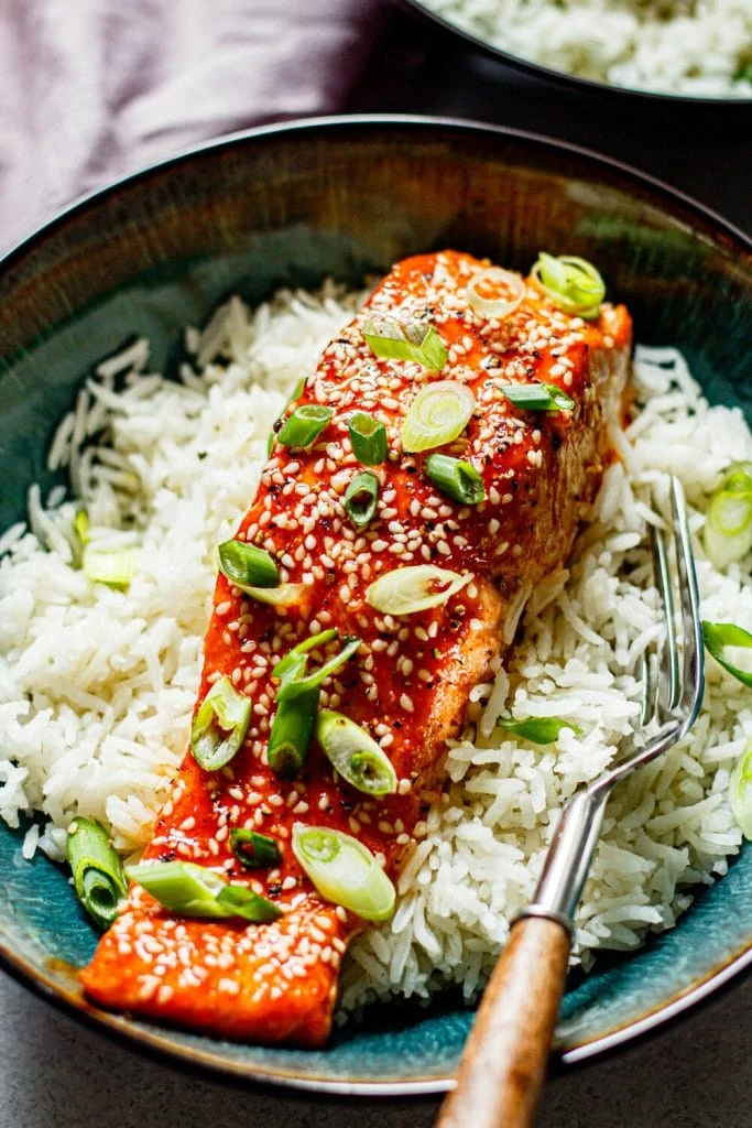 honey sriracha salmon on white rice in a bowl with a fork on the side