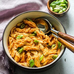shredded buffalo chicken in a brown bowl with two spoons