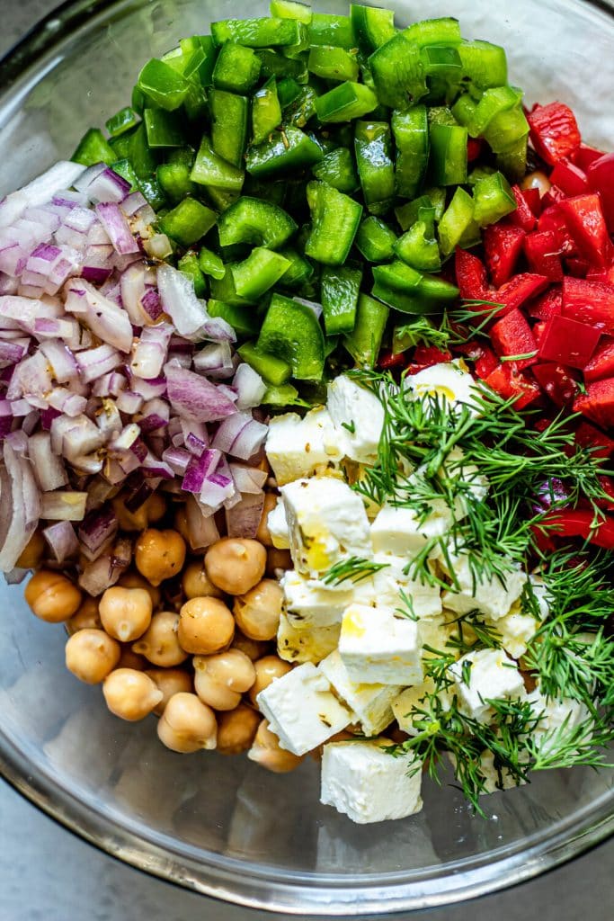 chickpeas, red onion, green pepper, red pepper, feta cheese, and dill in a glass mixing bowl