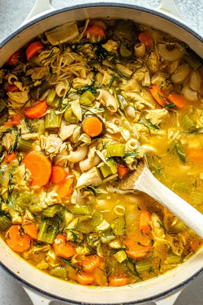 chicken noodle soup in cream dutch oven with wooden spoon