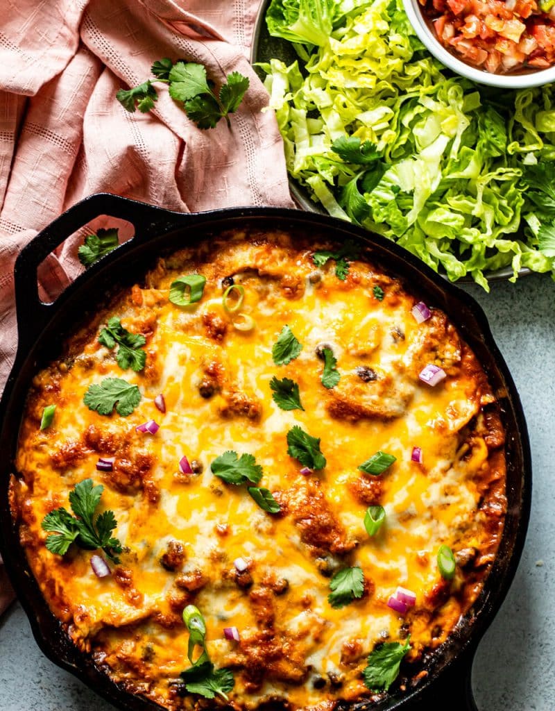 gluten free chicken enchiladas in a black cast iron skillet with a pink cloth and chopped lettuce