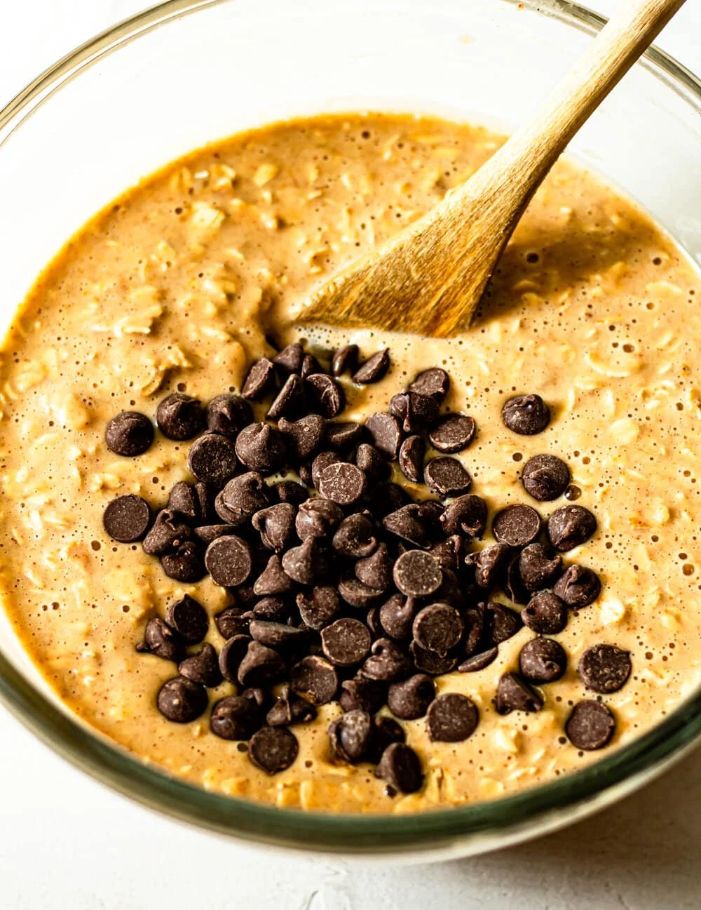 Peanut Butter Banana Baked Oatmeal cup batter in a glass bowl with wooden spoon and chocolate chips
