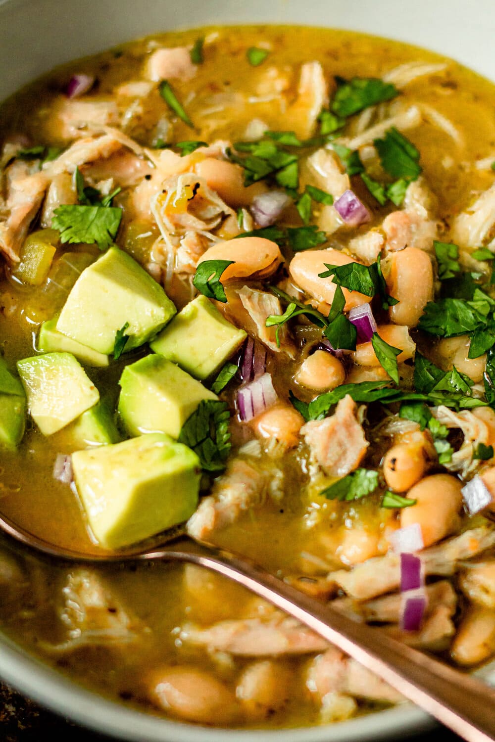 salsa verde soup in a white bowl with a gold spoon