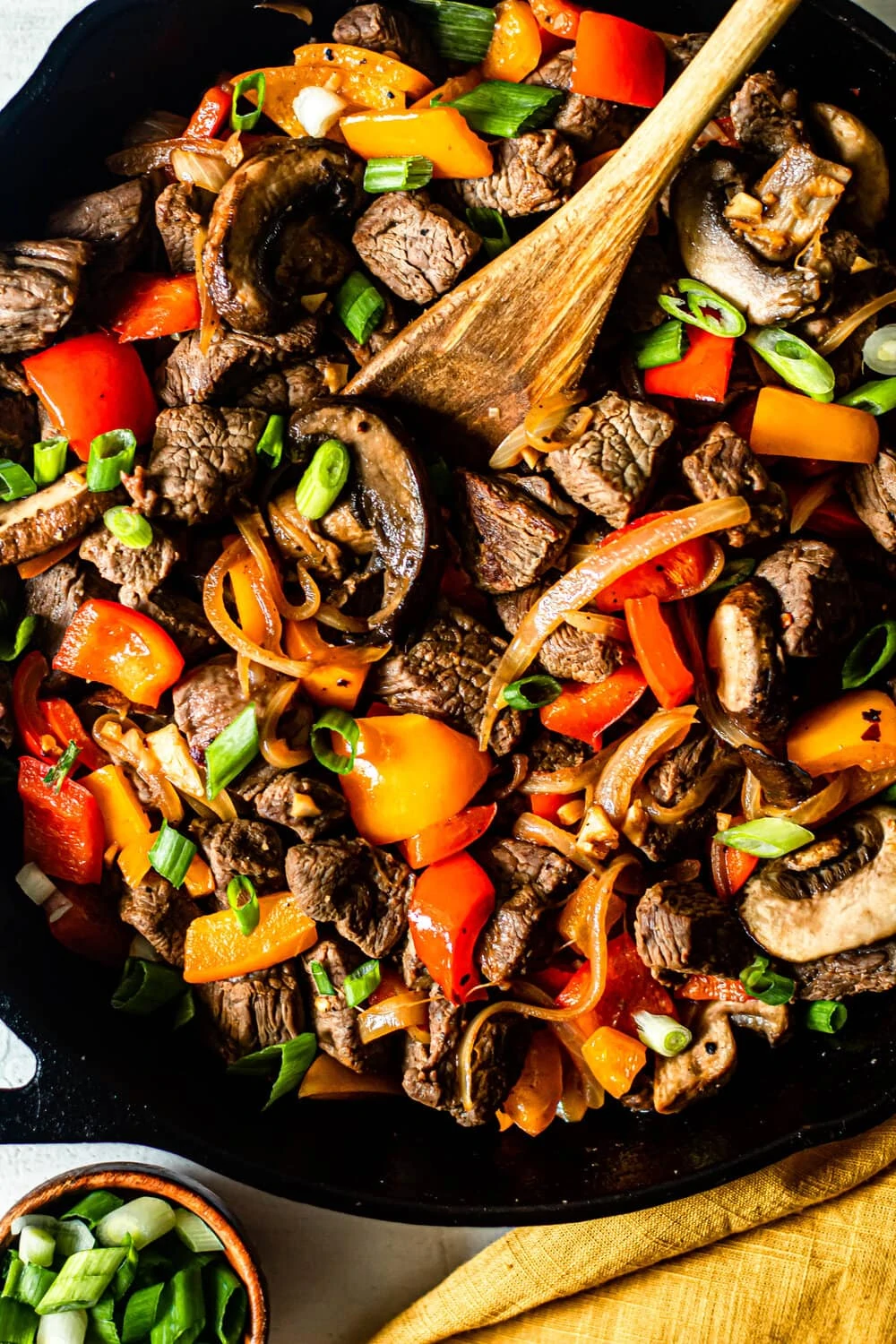 steak, peppers, and mushrooms with a wooden spoon in a cast iron skillet