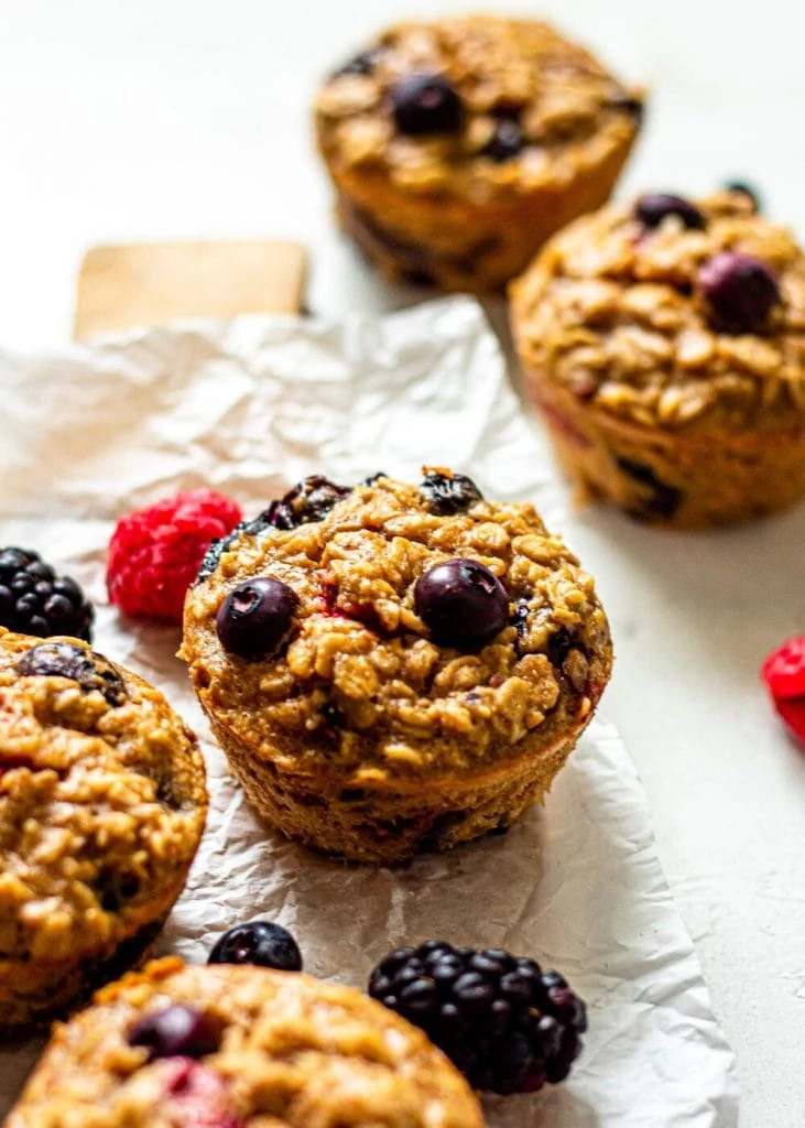 baked oatmeal cups on parchment paper surrounded by blueberries, raspberries, and blackberries