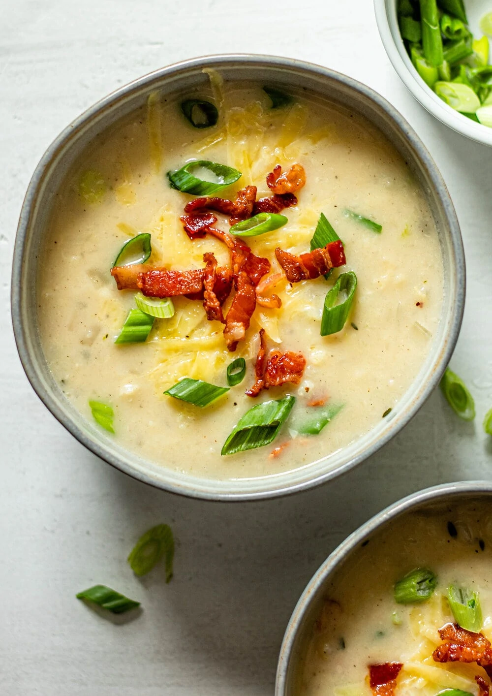 Loaded Cauliflower Soup in a grey bowl with bacon, green onions, and shredded cheese on top