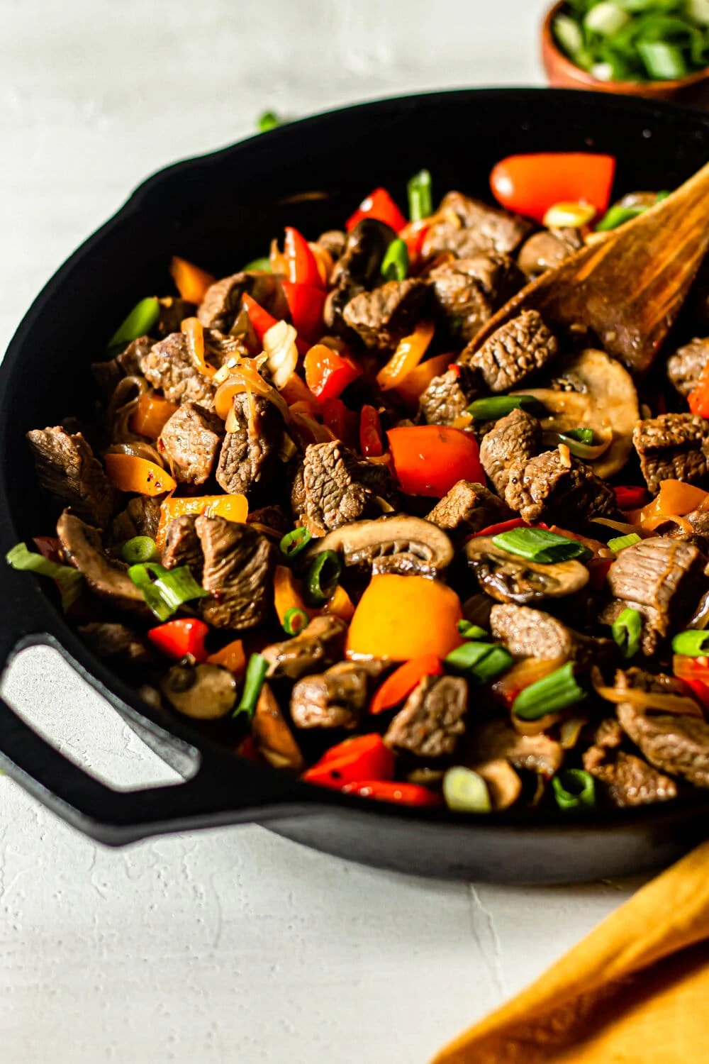 One Skillet Beef Tips with Peppers and Onions in cast iron skillet with wooden serving spoon