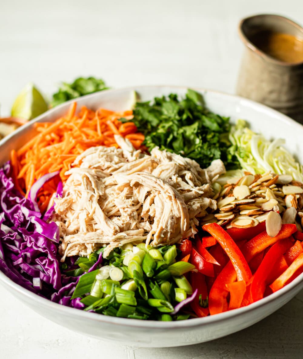 Thai Crunch Salad in white bowl with dressing in the background