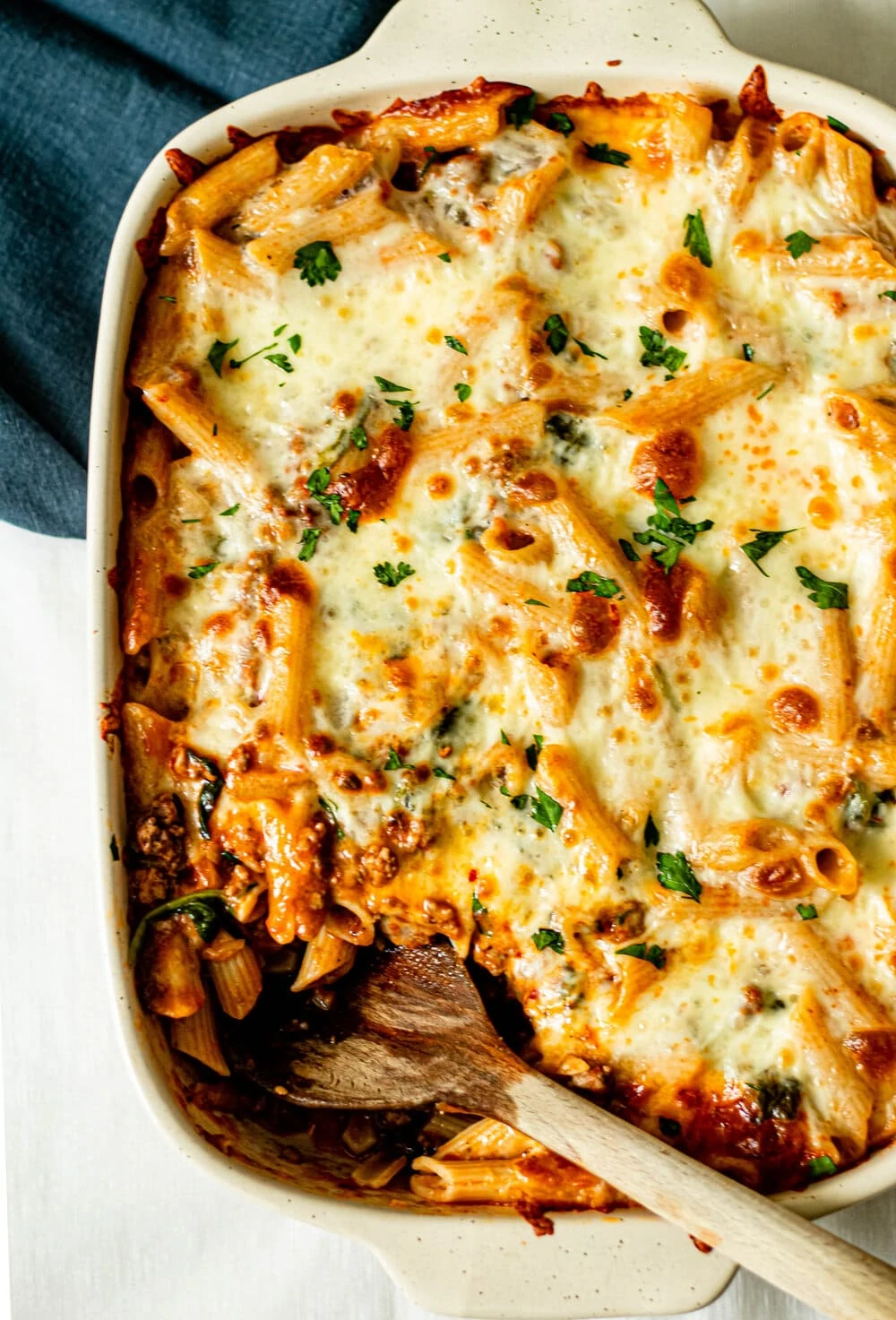 baked penne pasta in white baking dish with wooden serving spoon