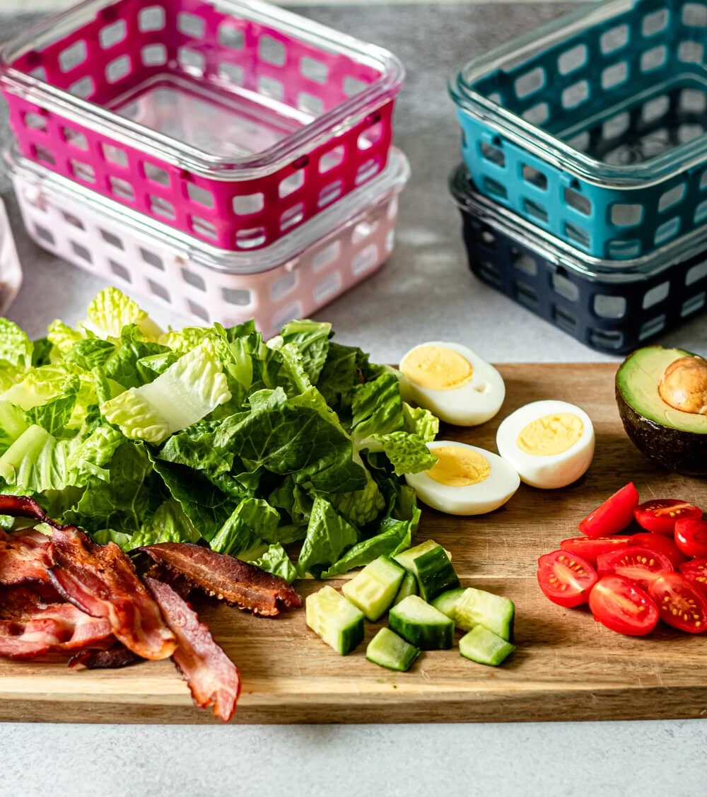 Easy Cobb Salad Meal Prep ingredients on a cutting board with meal prep containers in the background