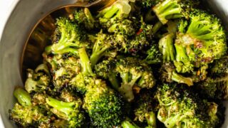 roasted garlic broccoli in a white bowl with gold spoon