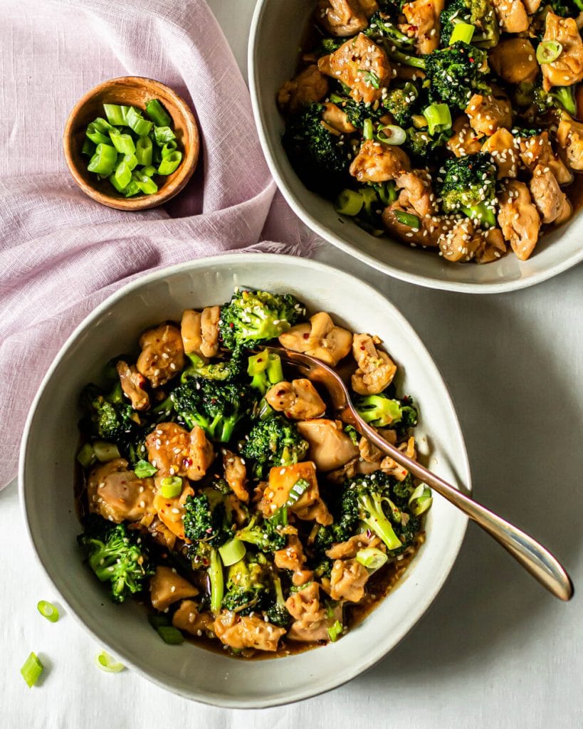 chicken and broccoli stir fry in grey bowls with purple cloth and fork