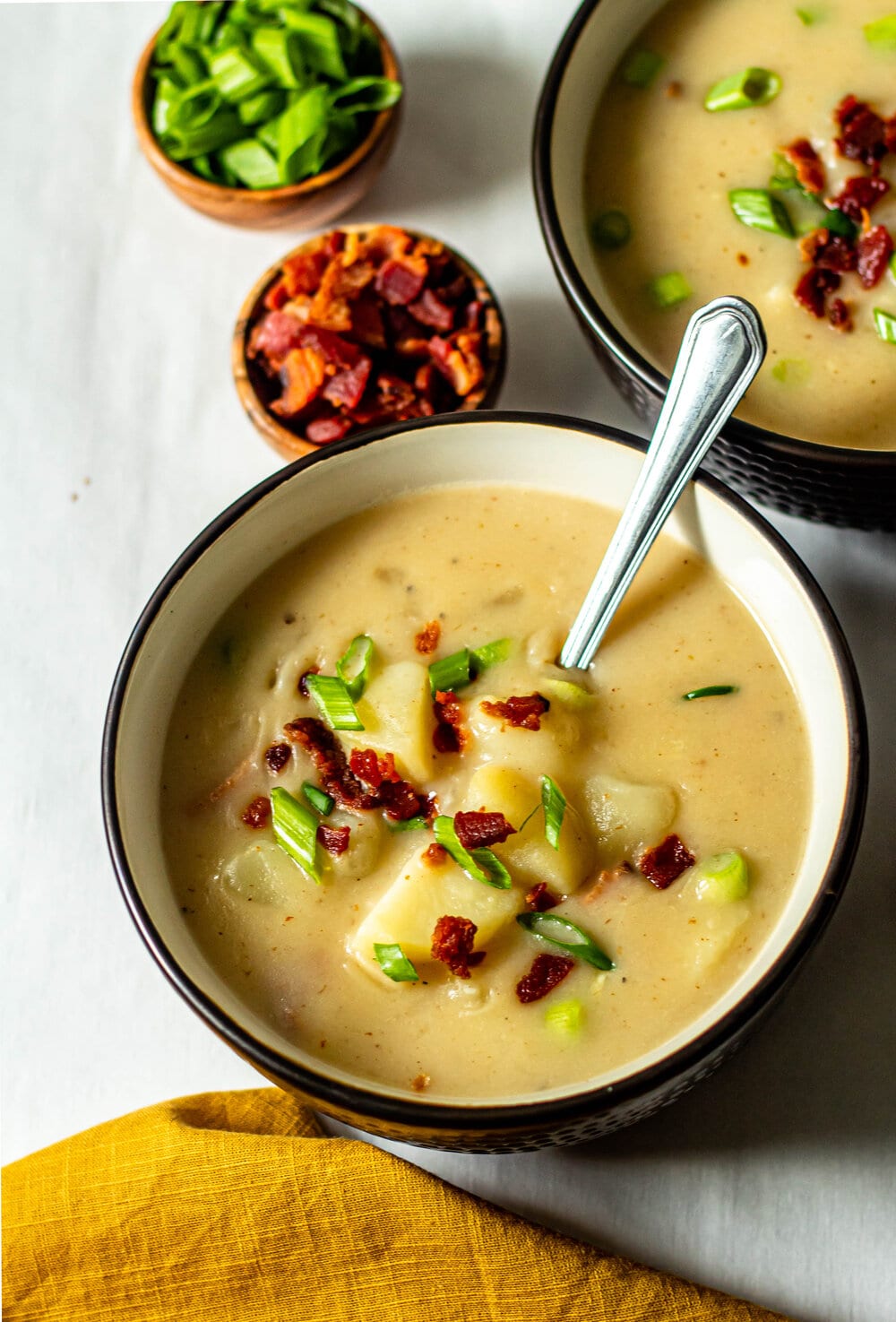 loaded baked potato soup in a brown bowl with a silver spoon and bacon and green onions sprinkled on top