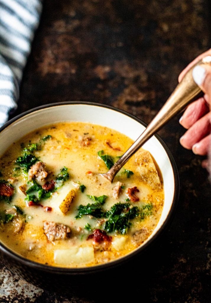 zuppa toscana soup in bowl with someone placing a spoon on the side