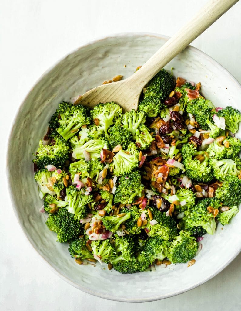 broccoli salad in a large white bowl with wooden spoon