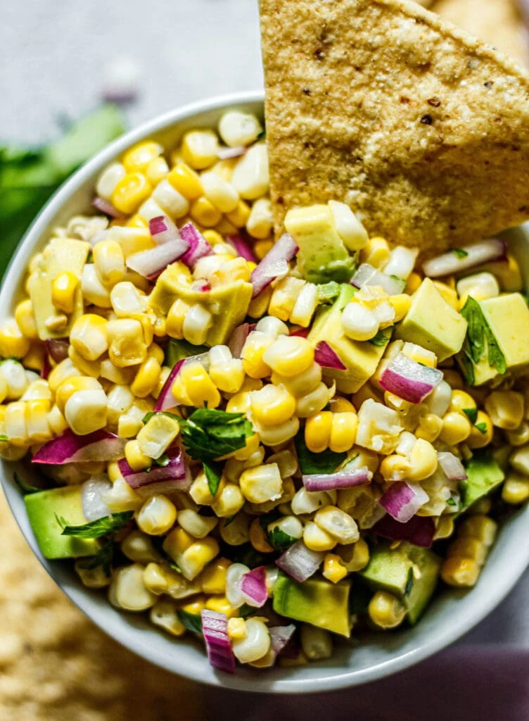 avocado corn salsa in a white bowl with tortilla chip dipped in the side of the salsa