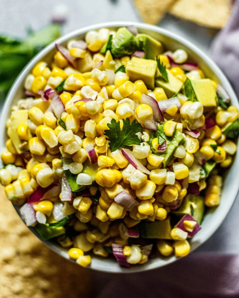 Avocado corn salsa in a white bowl with tortilla chips and cilantro sprinkled around the bowl