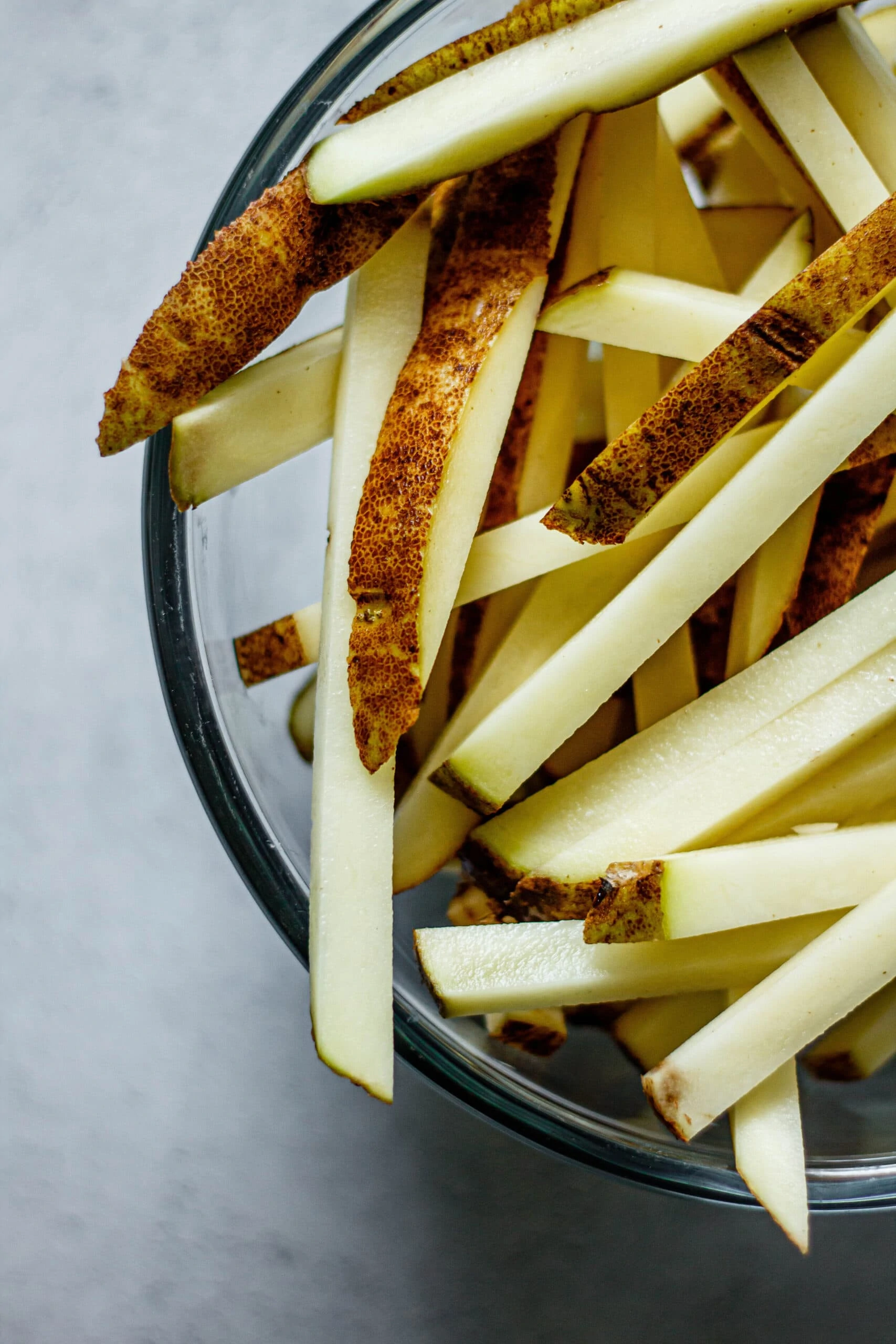 raw potatoes cut into French fries in glass mixing bowl
