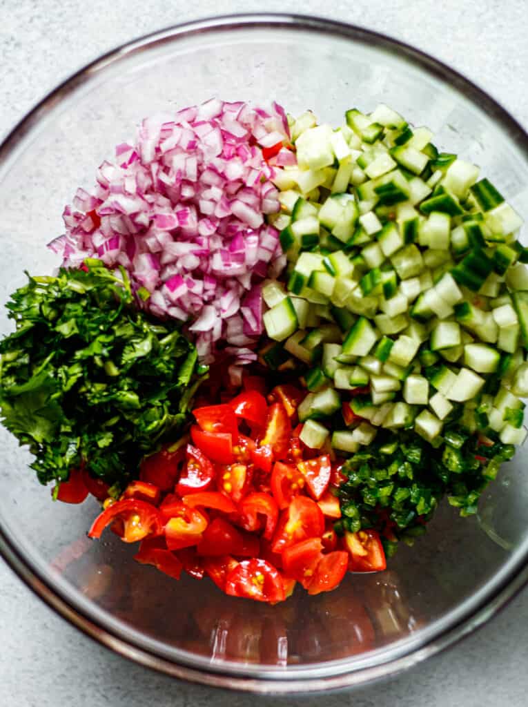 diced tomato, onion, cucumber, jalapeno, and cilantro in a clear mixing bowl