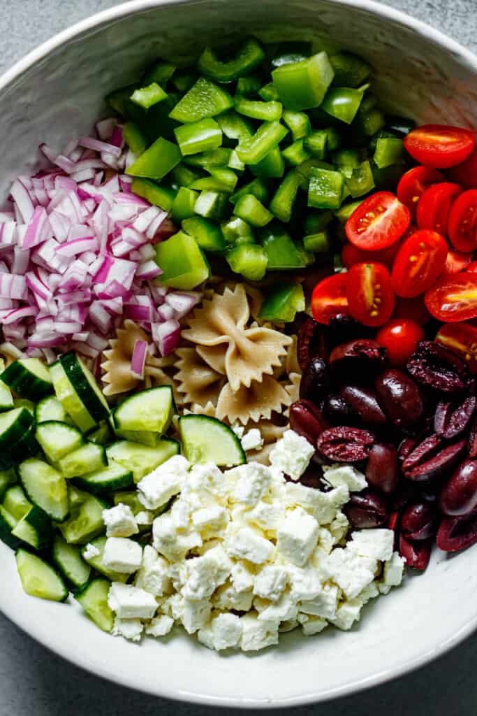 tomatoes, cucumbers, pasta, olives, red onion, and feta cheese in a large mixing bowl
