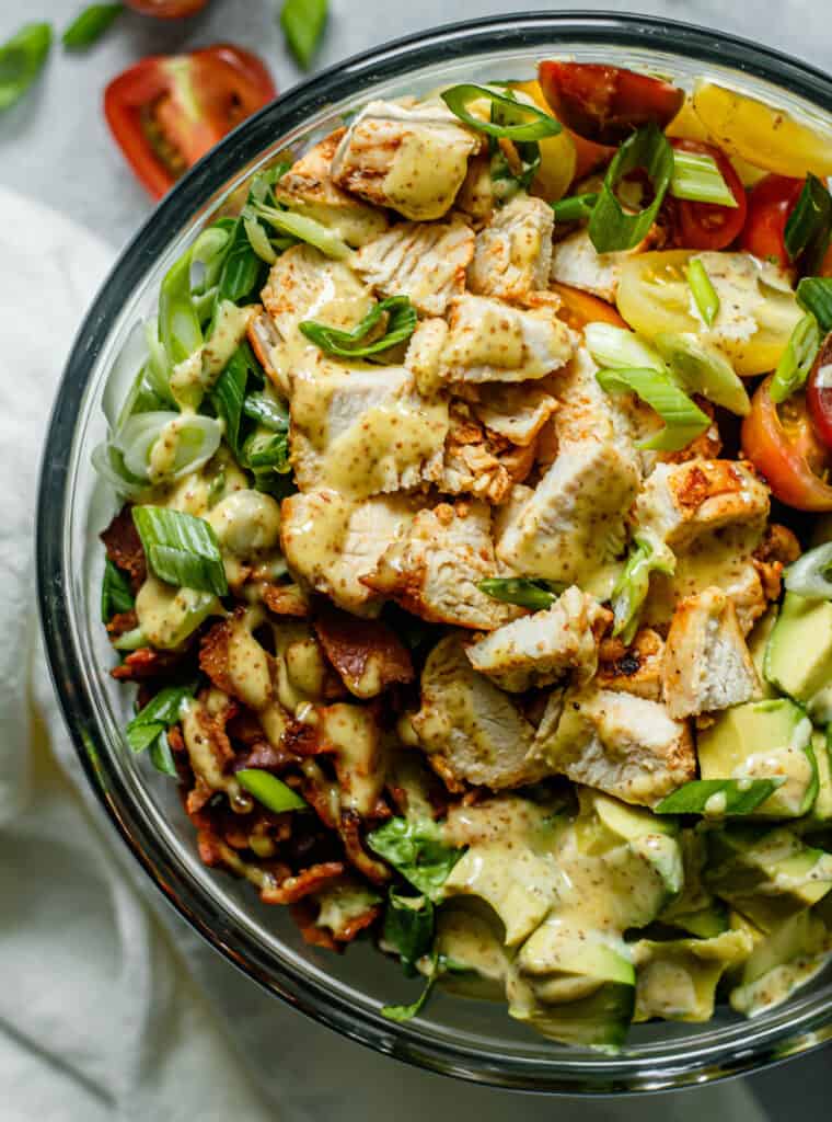 chicken, bacon, avocado, tomatoes, green onion, and honey mustard dressing in a glass mixing bowl