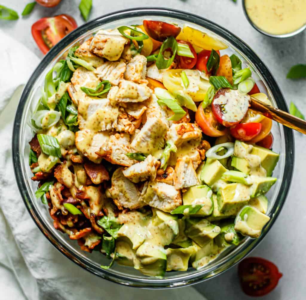 Huhn, Speck, Avocado, Tomaten, Römersalat und Frühlingszwiebeln in einer Glasschüssel mit Honig-Senf-Dressing