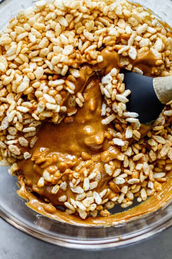 peanut butter and brown rice cereal in a glass mixing bowl with spatula