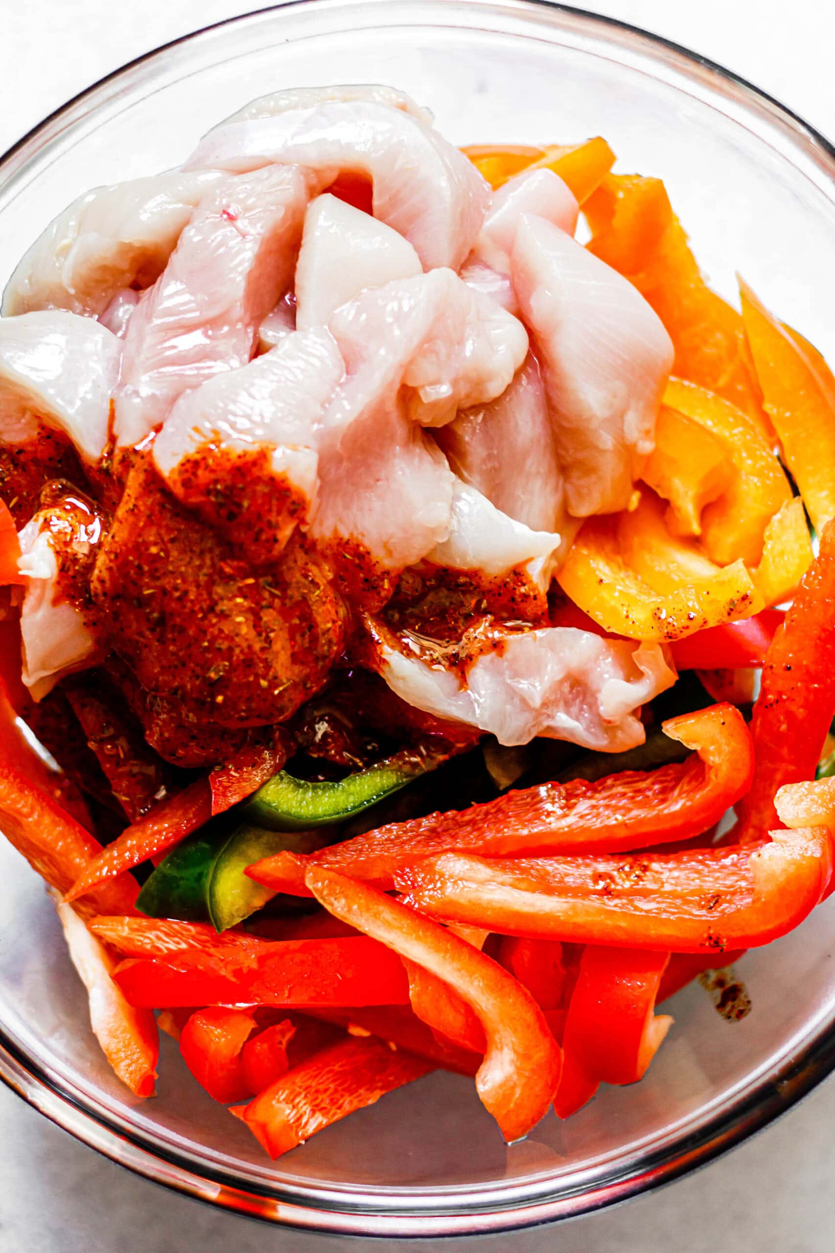 marinade, chicken, and peppers in a glass mixing bowl