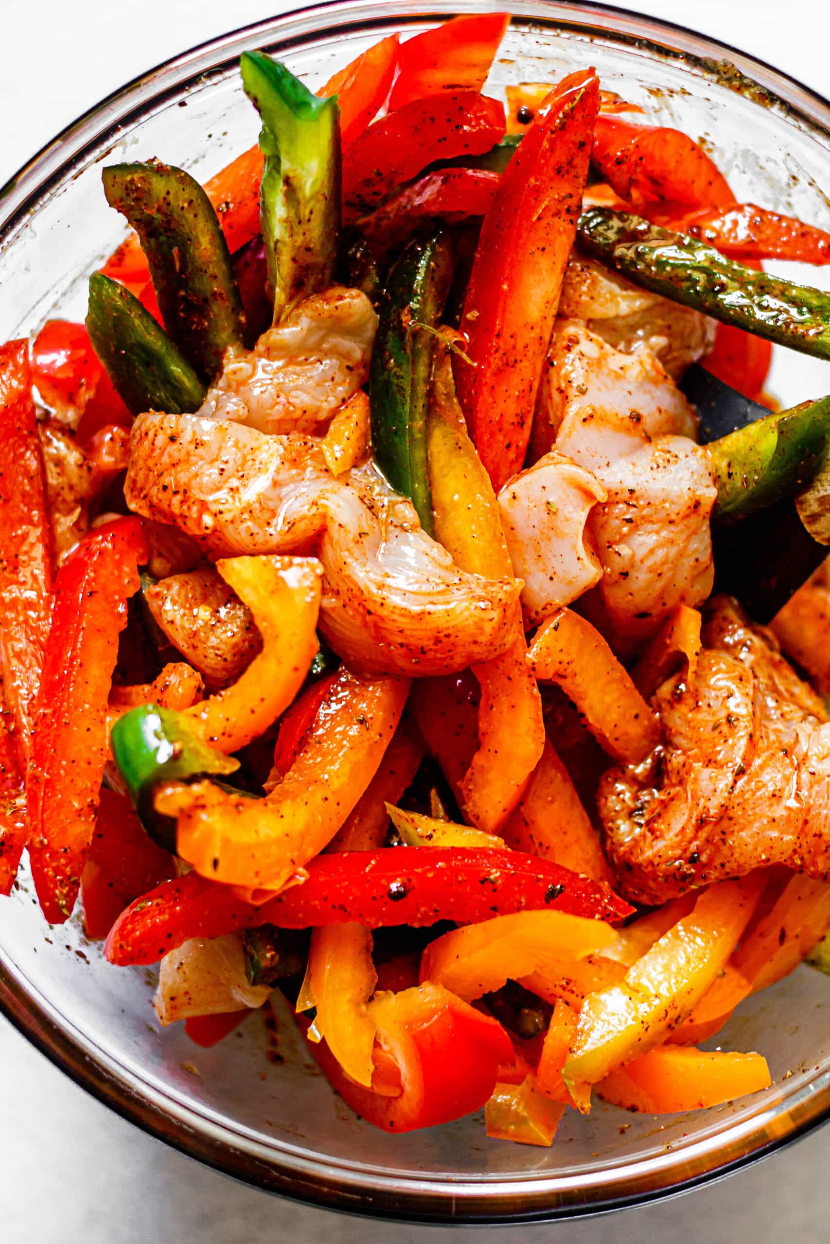 marinade, chicken, and peppers tossed together in glass mixing bowl