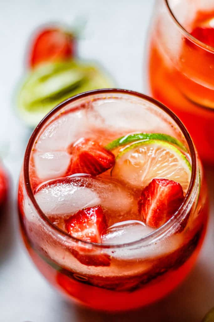 sparkling strawberry limeade in a glass with limes and strawberries in the background