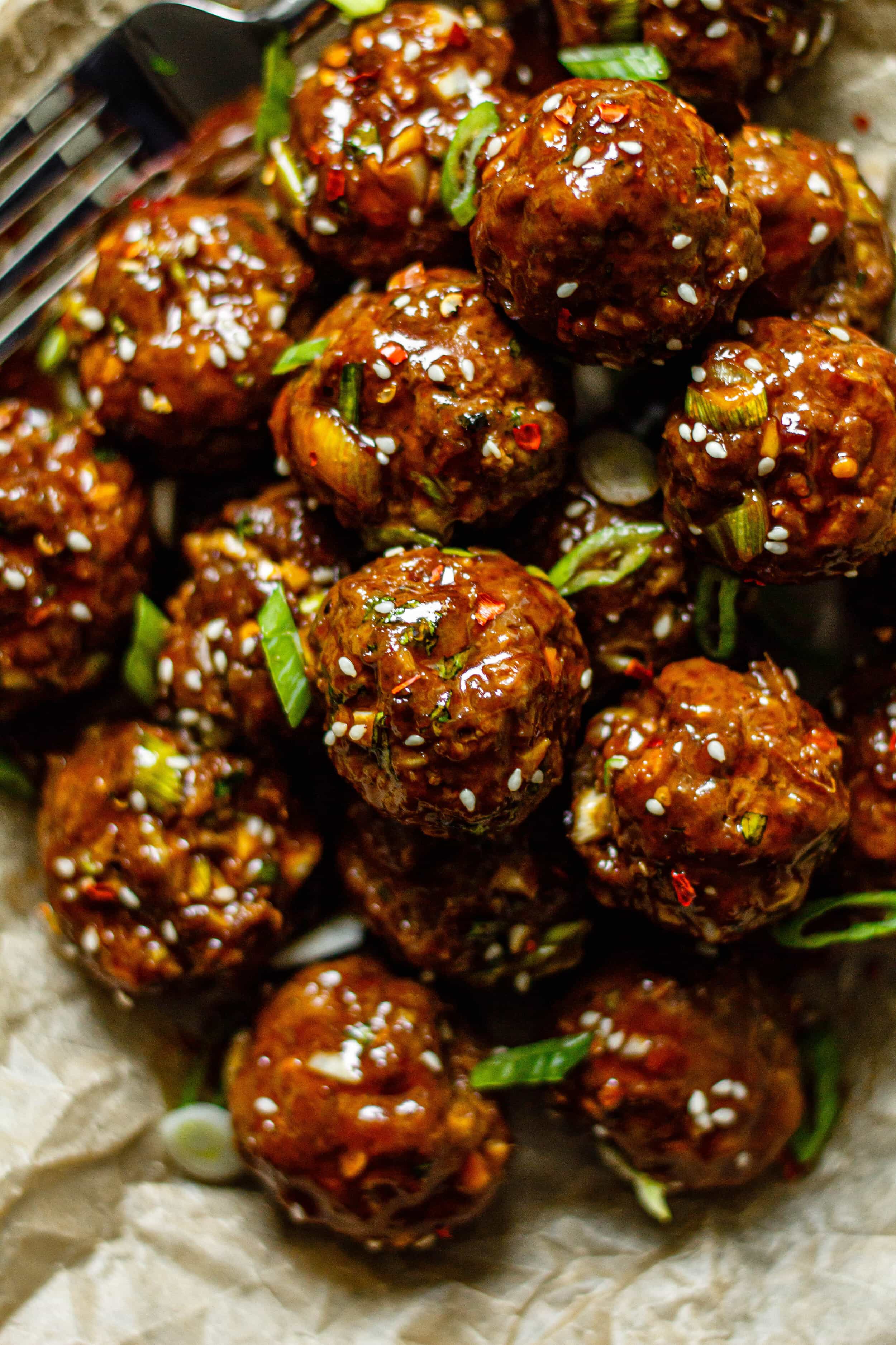 sticky ginger scallion meatballs on brown parchment paper topped with sesame seeds and green onion