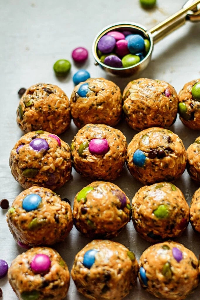 monster cookie energy bites on white parchment paper with chocolate candies and a cookie scoop in the background