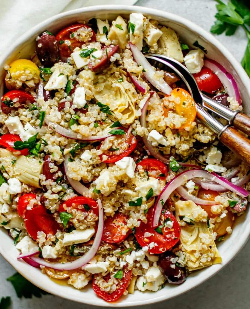 Mediterranean quinoa salad in a white bowl with two spoons