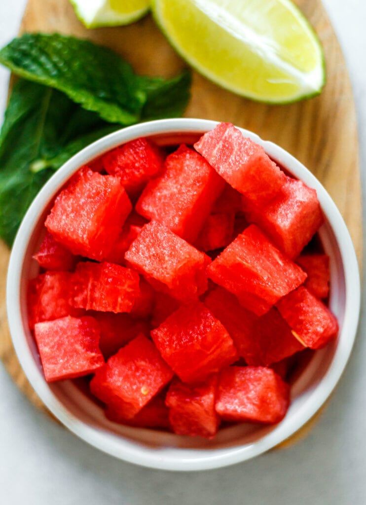 cubed watermelon, mint, and fresh limes on a wooden cutting board