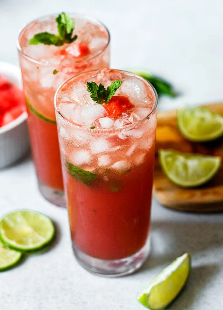 watermelon mojito in two tall glasses with limes and watermelon in the background