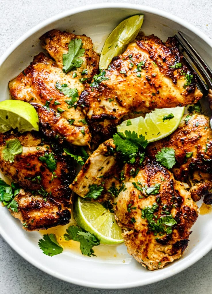 cilantro lime chicken thighs on white platter sprinkled with cilantro and lime slices