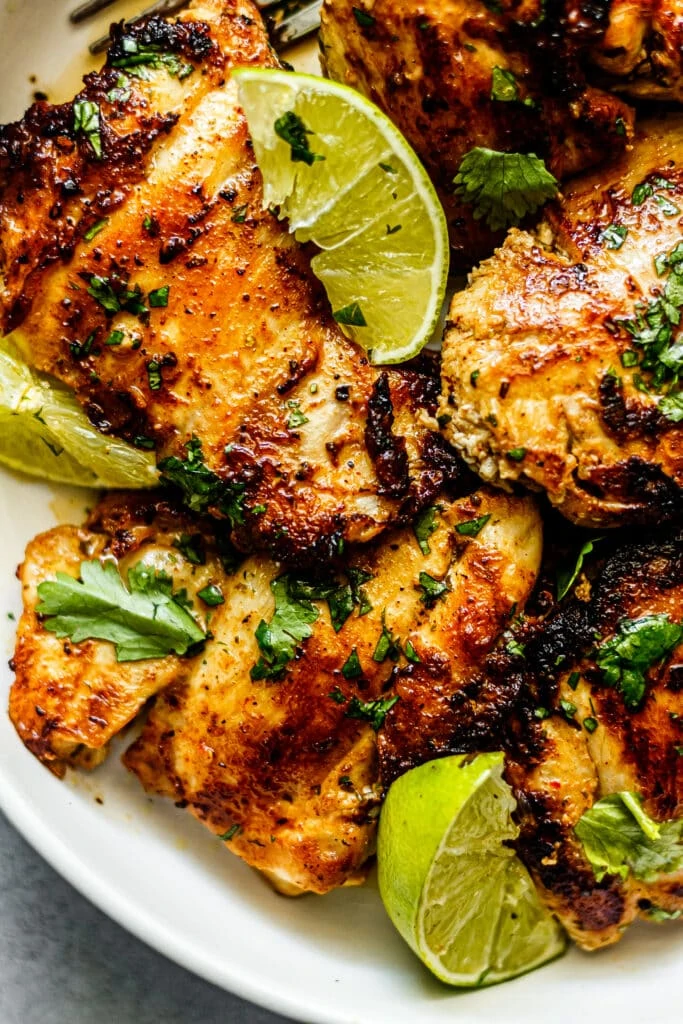 cilantro lime chicken thighs on white plate with lime slices and fresh cilantro
