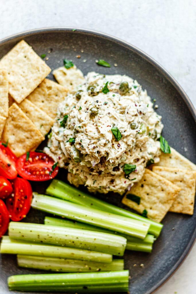 tuna salad, crackers, tomatoes, and celery on a grey plate