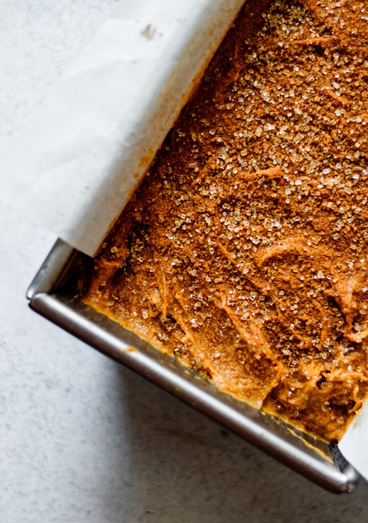 pumpkin bread batter sprinkled with cinnamon sugar in loaf pan with parchment paper