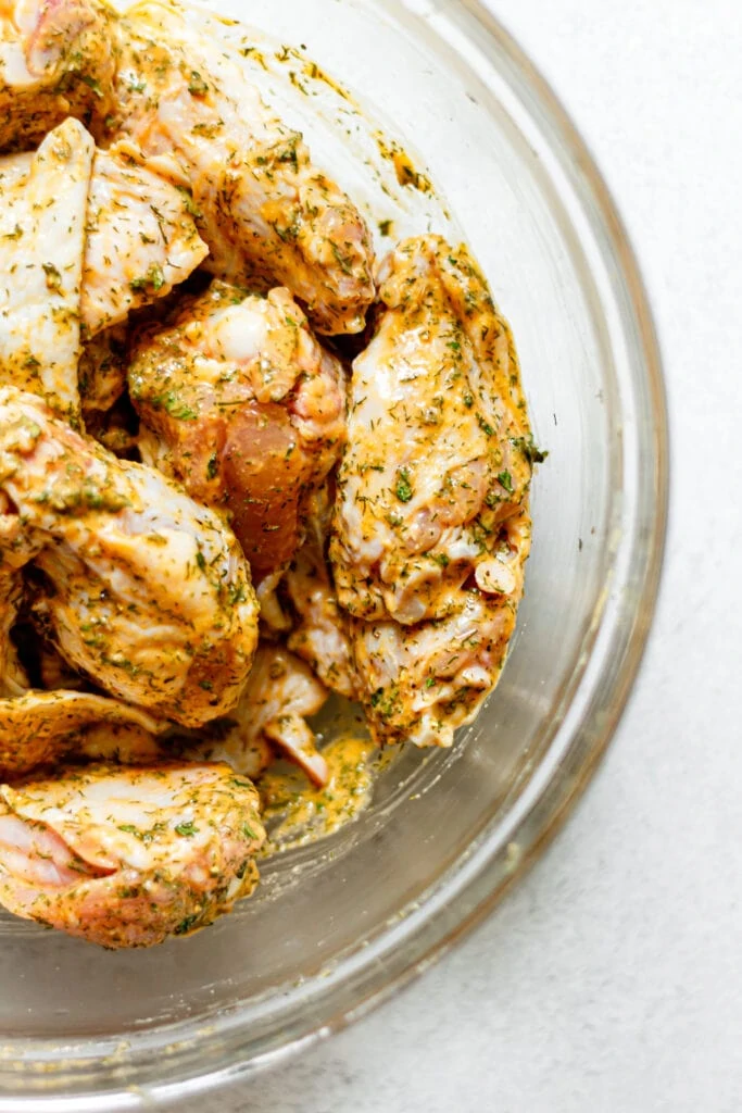 raw chicken wings with spices and seasonings in glass bowl