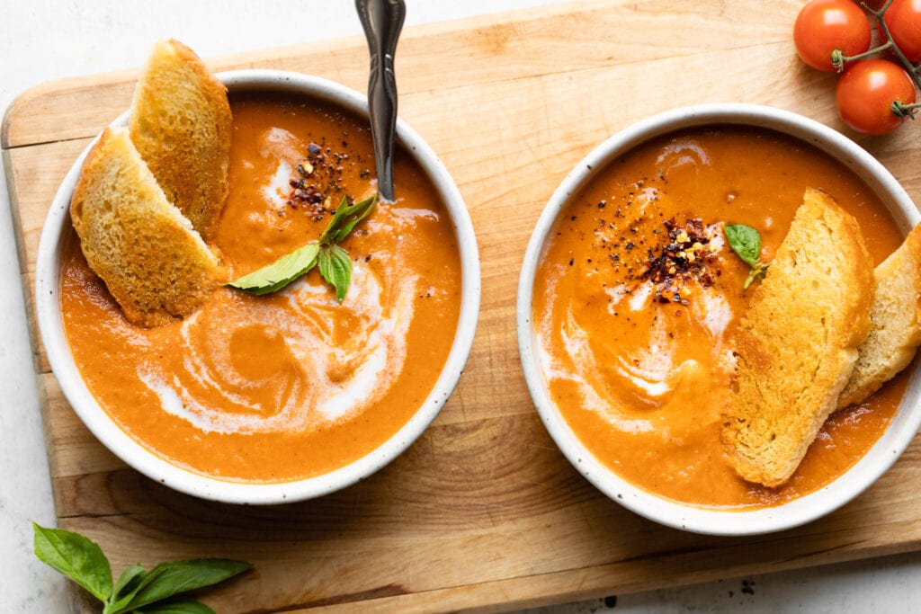 two bowls of tomato soup on wooden board